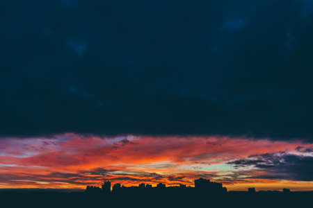 Cityscape with wonderful varicolored vivid dawn. Amazing dramatic multicolored cloudy sky above dark...