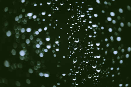 Dirty window glass with drops of rain. Atmospheric green background with raindrops in bokeh. Droplets and stains close up. Detailed transparent texture in macro with copy space. Rainy weather.の写真素材