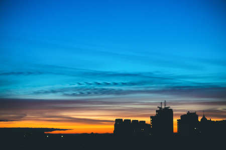Cityscape with wonderful varicolored vivid dawn. Amazing dramatic blue sky with purple and violet clouds above dark silhouettes of city buildings. Atmospheric background of orange sunrise. Copy space.の写真素材