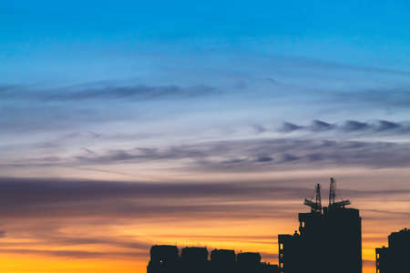Cityscape with wonderful varicolored vivid dawn. Amazing dramatic blue sky with purple and violet clouds above dark silhouettes of city buildings. Atmospheric background of orange sunrise. Copy space.の写真素材