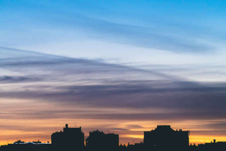 Cityscape with wonderful varicolored vivid dawn. Amazing dramatic blue sky with purple and violet clouds above dark silhouettes of city buildings. Atmospheric background of orange sunrise. Copy space.の写真素材