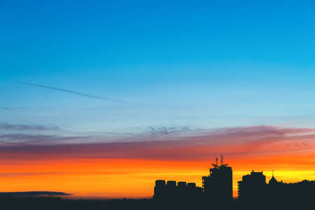 Cityscape with wonderful varicolored vivid dawn. Amazing dramatic multicolored cloudy sky above dark silhouettes of city buildings. Atmospheric background of sunrise. Orange sunlight. Copy space.の写真素材