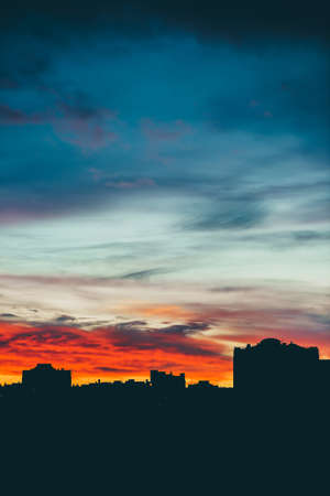Cityscape with wonderful varicolored vivid dawn. Amazing dramatic multicolored cloudy sky above dark silhouettes of city buildings. Atmospheric background of sunrise in overcast weather. Copy space.の写真素材