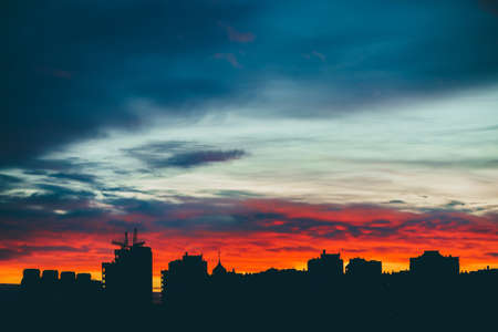 Cityscape with wonderful varicolored vivid dawn. Amazing dramatic multicolored cloudy sky above dark silhouettes of city buildings. Atmospheric background of sunrise in overcast weather. Copy space.の写真素材