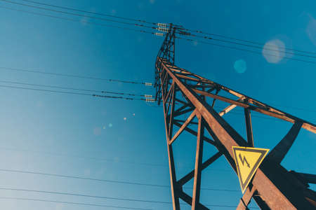 Power lines on background of blue sky close-up. Electric hub on pole. Electricity equipment with copy space. Wires of high voltage in sky. Electricity industry. Tower with lightning warning sign.