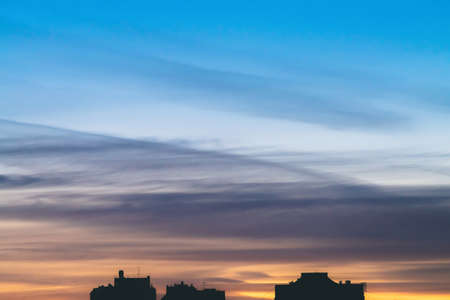 Cityscape with wonderful varicolored vivid dawn. Amazing dramatic blue sky with purple and violet clouds above dark silhouettes of city buildings. Atmospheric background of orange sunrise. Copy space.の写真素材