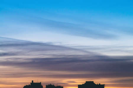Cityscape with wonderful varicolored vivid dawn. Amazing dramatic blue sky with purple and violet clouds above dark silhouettes of city buildings. Atmospheric background of orange sunrise. Copy space.の写真素材