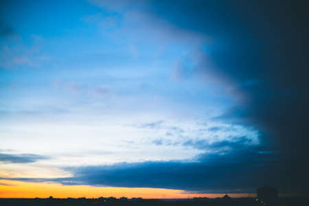 Cityscape with wonderful varicolored vivid dawn. Amazing dramatic blue cloudy sky above dark silhouettes of city buildings. Atmospheric background of orange sunrise in overcast weather. Copy space.の写真素材