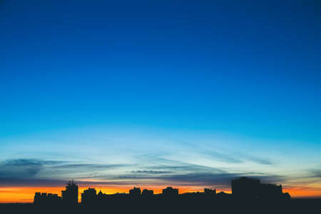 Cityscape with wonderful varicolored vivid dawn. Amazing dramatic blue sky with purple and violet clouds above dark silhouettes of city buildings. Atmospheric background of orange sunrise. Copy space.の写真素材