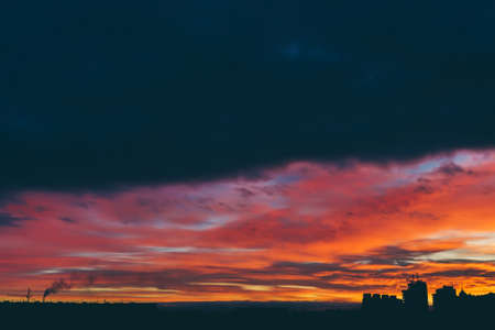 Cityscape with wonderful varicolored vivid dawn. Amazing dramatic multicolored cloudy sky above dark...