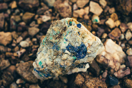 Raw ore on ground close-up. Multicolor rough stone in sunlight. Textured vivid geological background with pile of rude stones. Natural texture with copy space. Amazing mineral. Piece of rock.の写真素材