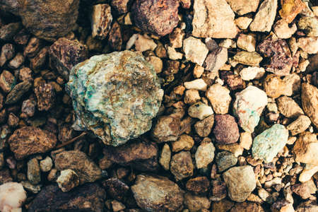 Raw ore on ground close-up. Multicolor rough stone in sunlight. Textured vivid geological background with pile of rude stones. Natural texture with copy space. Amazing mineral. Piece of rock.の写真素材