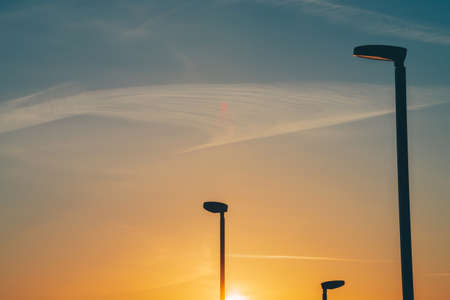 Special lanterns against light pollution at sunset close-up. Warm natural background of sky gradient of sunrise. Dawn with silhouettes of poles with street light. Minimalist predawn urban landscape.の写真素材