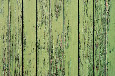 Old wooden painted rustic wall with green flaky dye. Faded wood planks close-up. Peeling paint on boards. Texture of damaged rough wooden of panels. Imperfect background. Weathered paint on old fence.の写真素材