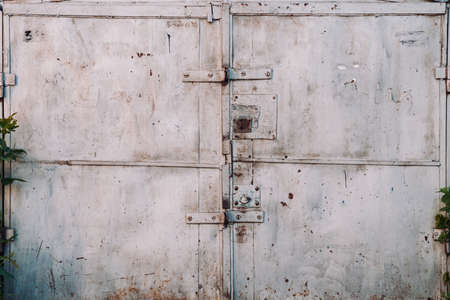 Closed imperfect rust metallic garage gate close-up. Damage texture of locked rusty iron door. Grungy metal surface. Textured background of rough faded uneven steel gates. Obsolete metal surface.の写真素材