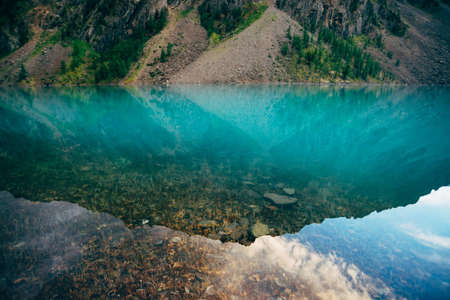 Plants and stones on bottom of mountain lake with clean water close-up. Giant mountain range...