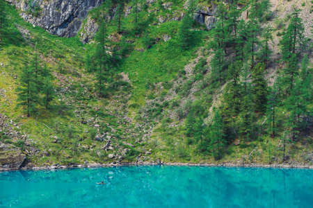 View above fisherman in boat on azure water of mountain lake. Fishing on highlands. Giant mountainside with forest in sunlight. Atmospheric minimalist beautiful landscape of nature in sunny day.の写真素材