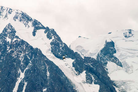 Helicopter in air against background of snowy mountain peak. Rescue mission in glaciers. Aerial tourism in highlands. Atmospheric view on mountain ridge in overcast weather. Icy rock close up.の写真素材