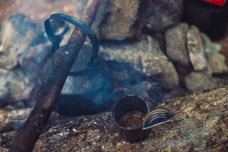 Extinguished bonfire with kettle on large firewood. Extinct bonfire close-up. Abandoned camping in...