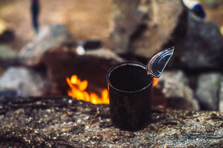 Heating of tea in metal mug on bonfire with large firewood. Tea drinking in open air. Active outdoor recreation. Camping in dusk. Romantic warm atmosphere in twilight on nature. Active rest.の写真素材