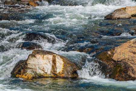 Big boulders in mountain creek close-up. Rapids of fast river with copy space. Foamed water stream....