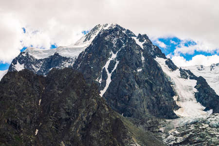 Amazing huge glacier top. Snowy mountain range in cloudy blue sky. Wonderful giant rocky ridge with...