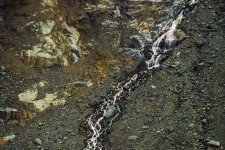 Detailed natural texture of slope from loose stones. Mountain water stream flows down mountainside....