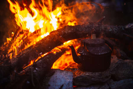 Boiling of tea in kettle on bonfire with large firewood. Tea drinking in open air. Active outdoor...
