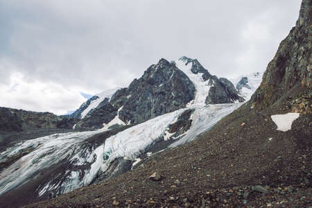 Snow on mountain range. Atmospheric snowy ridge under cloudy sky. Unusual giant rocks in overcast...