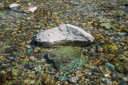 Varicolored detailed texture of stony bottom of transparent brook close up. Big boulder in clean water of mountain creek. Colorful background of smooth stones in river stream with copy space.の写真素材