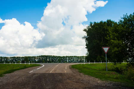 Road sign of give way on crossroads of dirt road before asphalt road. Landscape with highway and...
