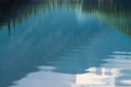 Shiny texture of surface of mountain lake. Background with reflection of green mountains with tops...