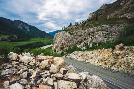 Highway across pass in mountains. Asphalt road near rocky cliff. Mountain river in valley. Amazing colorful highland landscape of majestic nature.の写真素材