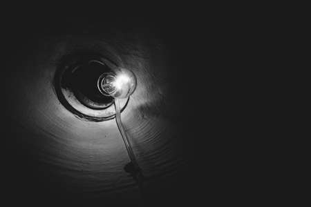 Incandescent lamp burns inside dark room close-up. Illumination. Old light bulb on rough wall. Lamp illuminate basement in grayscale. Light in darkness. Minimalist monochrome background. Copy space.の写真素材