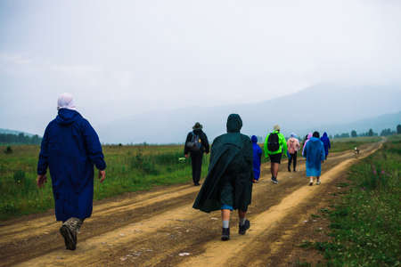 People go forward in mountain despite bad weather. Travelers goes upwards along road after dog. Way on foot in highlands in rainy overcast day. Summit despite everything. Walking in mountains.の写真素材
