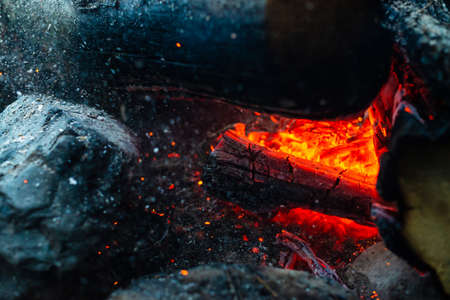 Smoldered logs burned in vivid fire close up. Atmospheric background with orange flame of campfire. Unimaginable detailed image of bonfire from inside with copy space. Smoke and glowing embers in air.の写真素材