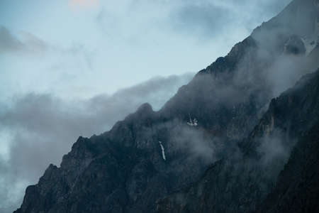 Ghostly giant rocks with trees in thick fog. Mysterious huge mountain with snow in mist. Early morning in mountains. Impenetrable fog. Dark atmospheric eerie landscape. Tranquil mystic atmosphere.の写真素材