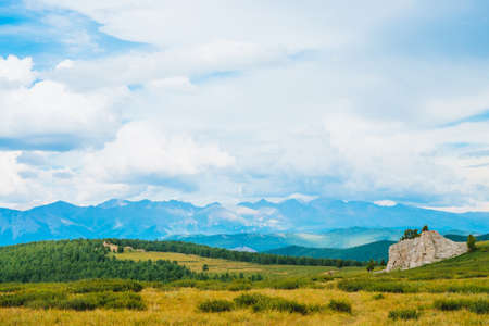 Spectacular view of mountain scenery. Landscape with footpath near rocky stone in highlands. Rock with trees and vegetation. Distant giant mountains under cloudy sky. Wonderful scenic mountainscape.の写真素材