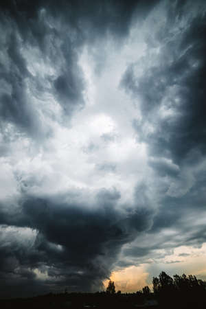 Dramatic cloudscape. Sunny light through dark heavy thunderstorm clouds before rain. Overcast rainy bad weather. Storm warning. Natural gray background of cumulonimbus. Sunlight in stormy cloudy sky.の写真素材