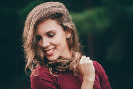 Beautiful girl with curly natural hair laugh in forest. Ð¡heerful lady in burgundy dress on green...