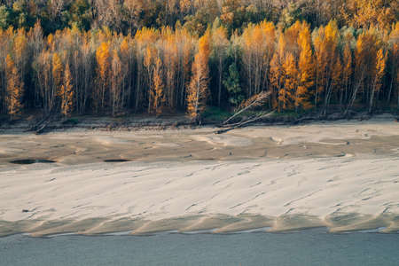 Wonderful autumn landscape with multicolor foliage. Scenic riverbank with fall leaves on trees. Scenery with yellow orange leafage. Beautiful golden autumn. Colorful fall forest. Grove near sandbank.の写真素材