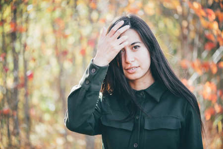 Female beauty portrait surrounded by vivid foliage. Dreamy beautiful girl with long natural black hair on autumn background with colorful leaves in bokeh. Inspired girl enjoys nature in autumn forest.の写真素材