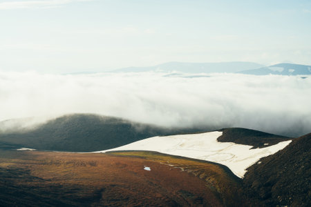 Atmospheric alpine landscape with giant low cloud above rocky mountain with glacier. Big thick cloud above highland valley. Wonderful scenery on high altitude. Flying over mountains above clouds.の写真素材