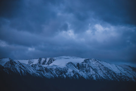 Atmospheric alpine darker landscape to snowy mountain ridge in dusk. Wonderful overcast scenery with...