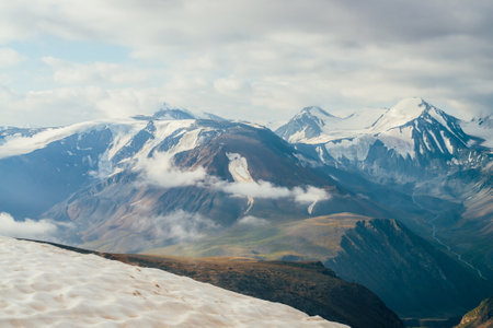 Atmospheric alpine landscape with snow on peak and big snowy mountains. Low clouds above valley among giant mountain ridges. Wonderful highland scenery with massive glacier on huge mountain range.の写真素材