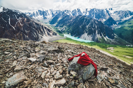 Vivid red mountaintop tour on peak overlooking scenic valley with big beautiful mountain lake surrounded by giant rocky ranges and glaciers. Man-made stony pile on top. Majestic wilderness nature.の写真素材