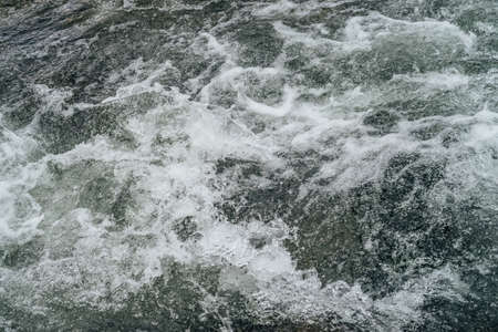Full frame nature background of water riffle of mountain river. Powerful water stream of mountain creek with rapids. Natural textured backdrop of fast flow of mountain brook. Rapids texture close-up.の写真素材