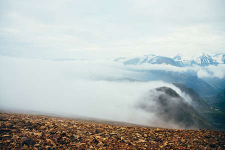 Atmospheric alpine landscape to giant low cloud above rocky mountains. Big thick clouds above highland valley. Wonderful scenery on high altitude. View from slope on snowy mountain range with glacier.の写真素材