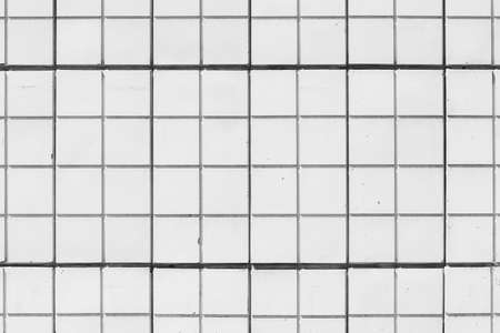 Minimalist background of white tiled building wall. Square tiles on house side close-up. Backdrop of white imperfect wall of old building. Unideal side of house of tile. Textured surface of facade.の写真素材