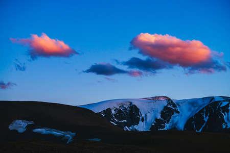 Atmospheric dawn landscape with silhouettes of snowy mountains with glaciers under sunset sky with...